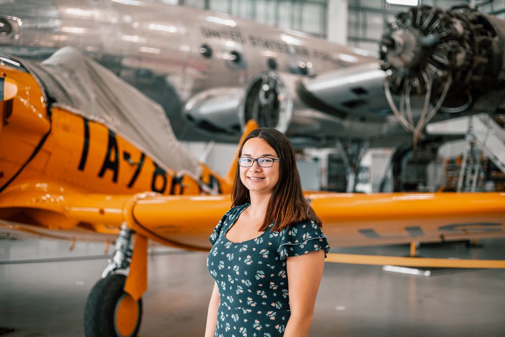 Bridgewater College student Jen Chan pictured at her internship site, Dynamic Aviation in Bridgewater. She is smiling and a plane is visible behind her.