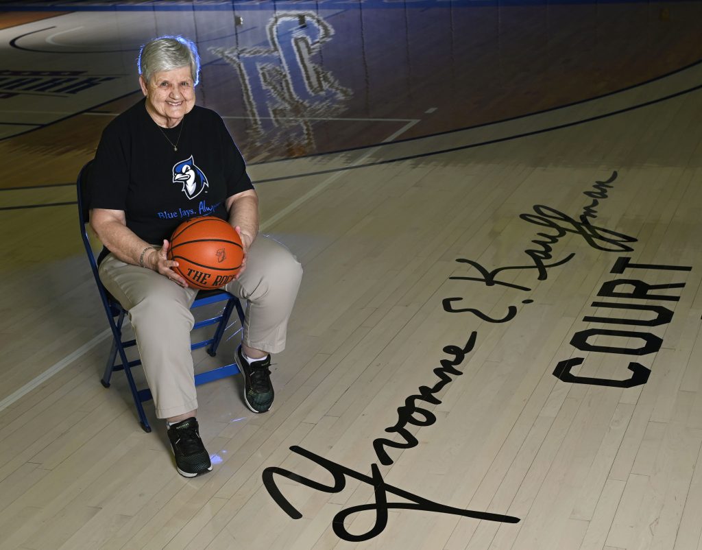 Yvonne Kauffman sitting in a chair holding a basketball on the court at Elizabethtown College that bears her name: Yvonne E. Kauffman Court.