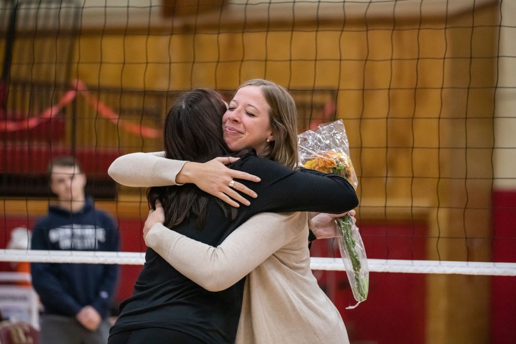 Women's volleyball coach Erin Harris hugs a student on the court